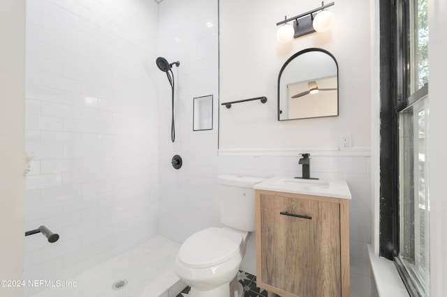 bathroom featuring vanity, toilet, tiled shower, and tile walls