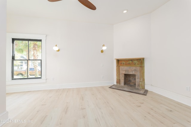 unfurnished living room with light wood-type flooring, a stone fireplace, and ceiling fan