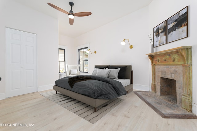 bedroom with ceiling fan, a fireplace, and light hardwood / wood-style floors