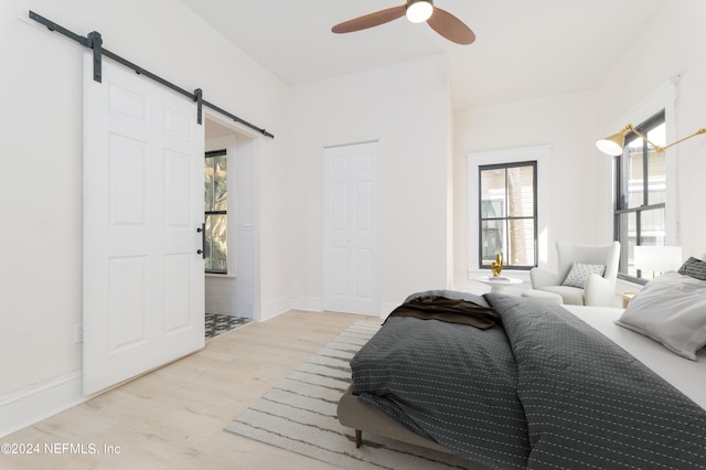 bedroom with a barn door, ceiling fan, and light wood-type flooring