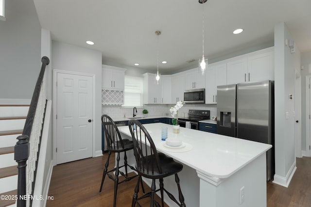 kitchen featuring white cabinets, a kitchen island, a sink, stainless steel appliances, and backsplash