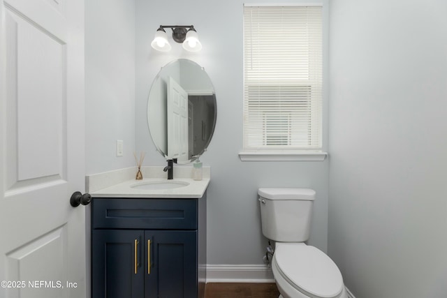 half bath featuring baseboards, vanity, and toilet