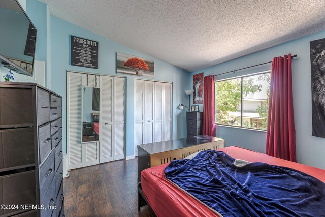 bedroom with lofted ceiling, a textured ceiling, multiple closets, and dark hardwood / wood-style flooring