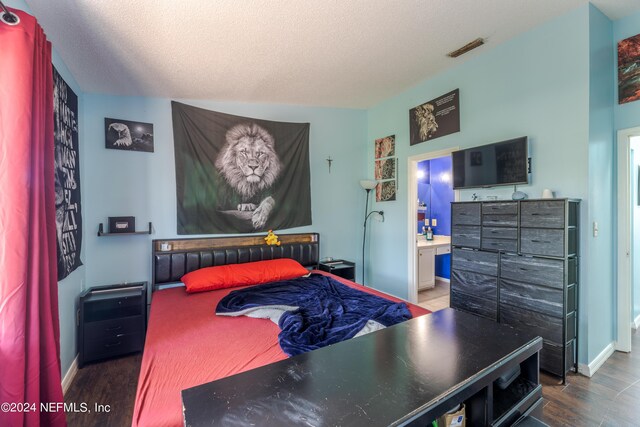 bedroom featuring lofted ceiling, hardwood / wood-style flooring, ensuite bathroom, and a textured ceiling