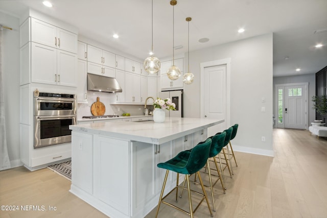 kitchen with white cabinets, appliances with stainless steel finishes, a large island with sink, and light hardwood / wood-style flooring