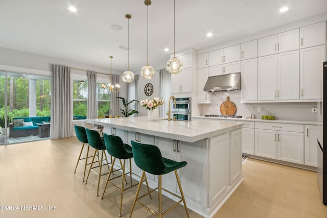 kitchen featuring decorative light fixtures, a kitchen island with sink, and white cabinets