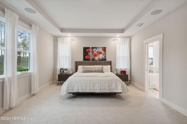 bedroom with light carpet, connected bathroom, and a tray ceiling