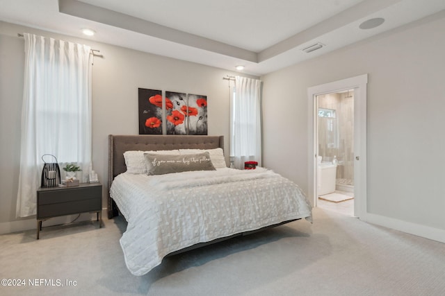 carpeted bedroom featuring a tray ceiling and ensuite bathroom