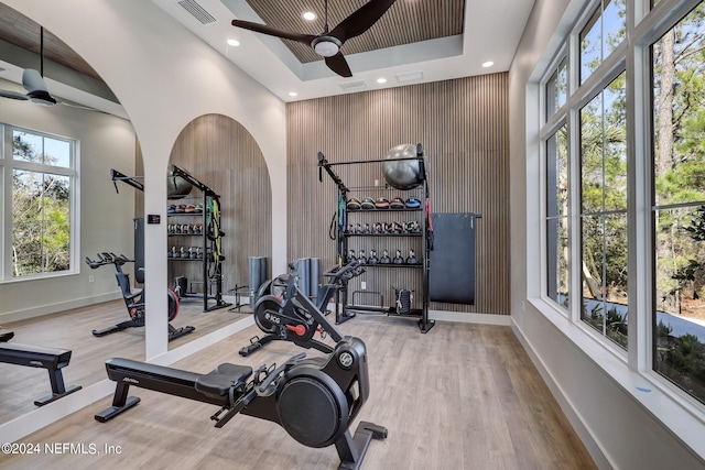 workout room with a towering ceiling, a tray ceiling, ceiling fan, and hardwood / wood-style flooring