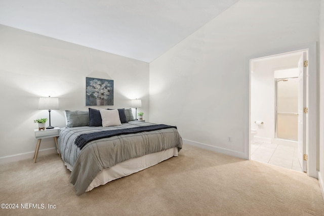 bedroom featuring light carpet, lofted ceiling, and ensuite bathroom