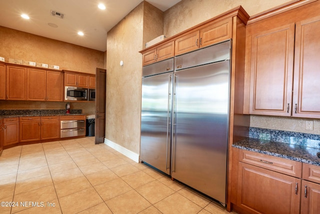 kitchen with dark stone countertops, built in appliances, and light tile patterned floors