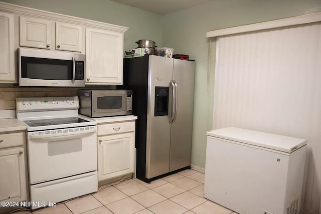 kitchen with appliances with stainless steel finishes, light tile patterned floors, white cabinetry, and decorative backsplash