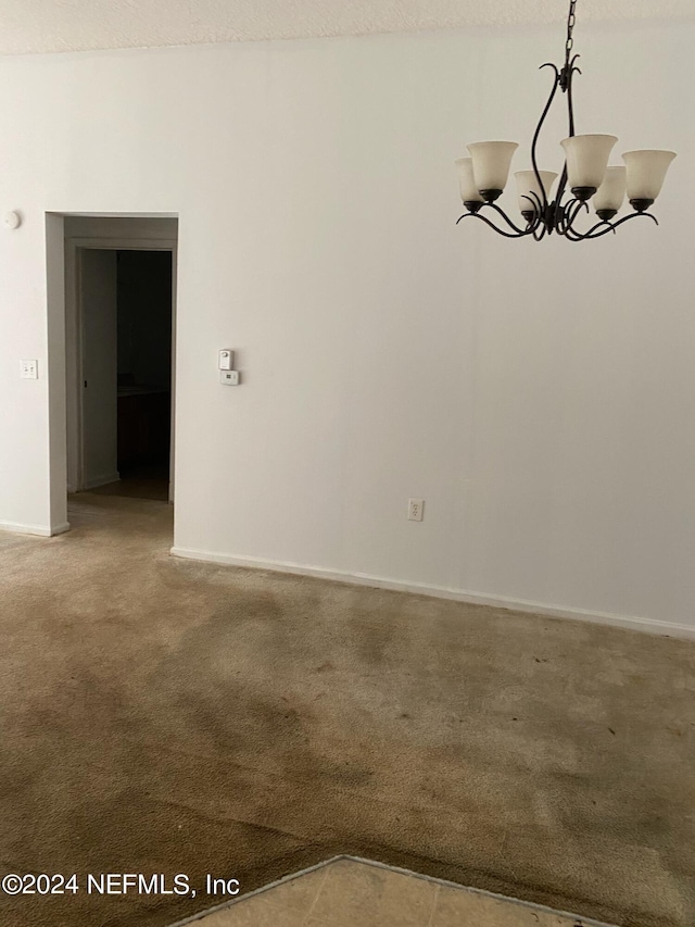 carpeted empty room featuring a chandelier