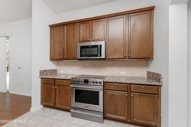 kitchen with light stone countertops, appliances with stainless steel finishes, decorative backsplash, and light tile patterned flooring