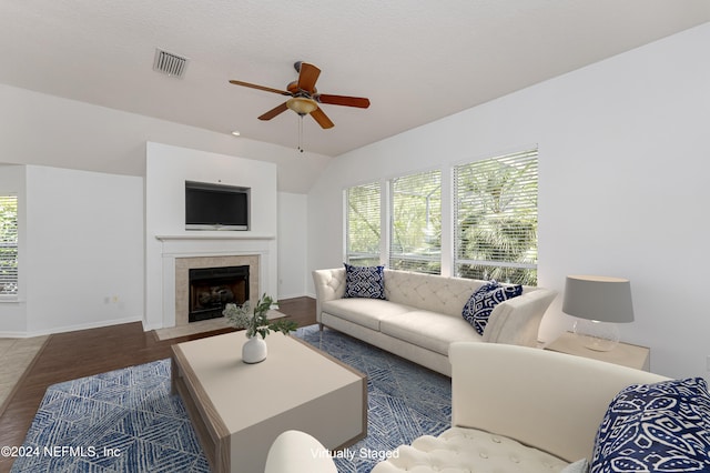 living room featuring a textured ceiling, vaulted ceiling, ceiling fan, a tile fireplace, and wood-type flooring