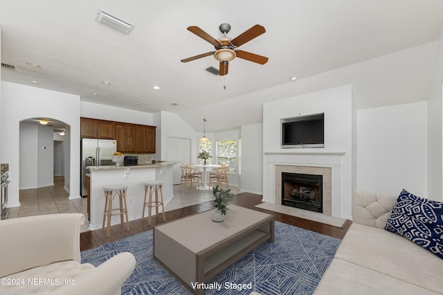 living room with a tile fireplace, ceiling fan, dark wood-type flooring, and lofted ceiling