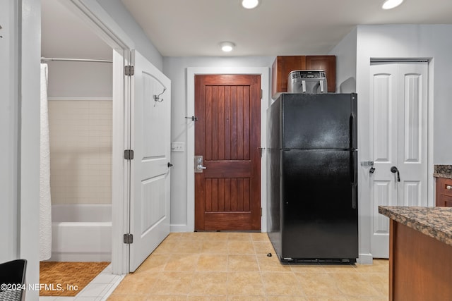 kitchen featuring dark stone countertops, light tile patterned flooring, and black refrigerator