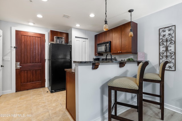 kitchen featuring pendant lighting, light tile patterned floors, kitchen peninsula, black appliances, and a breakfast bar