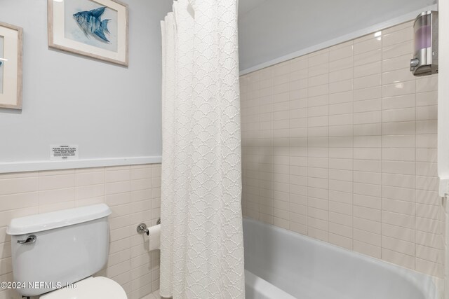 bathroom with shower / tub combo with curtain, tile walls, and toilet