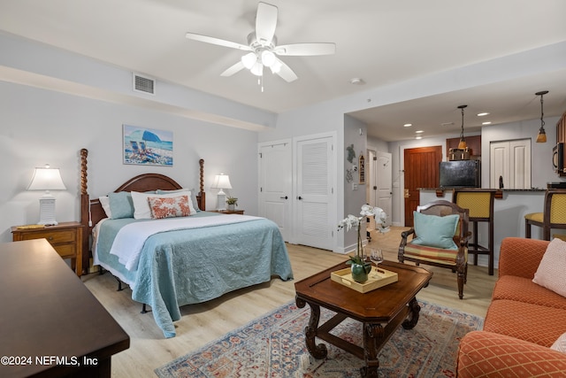 bedroom with ceiling fan, black fridge, two closets, and light hardwood / wood-style floors