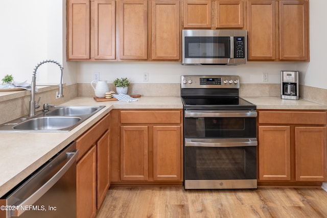 kitchen with appliances with stainless steel finishes, sink, and light hardwood / wood-style flooring