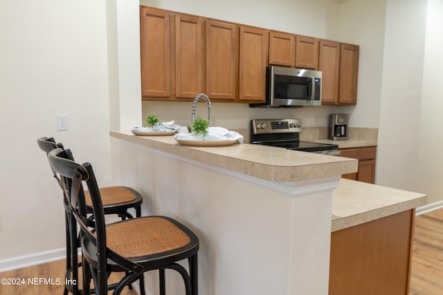 kitchen featuring light hardwood / wood-style flooring, stainless steel appliances, kitchen peninsula, and a breakfast bar area