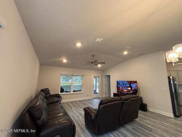 living room featuring vaulted ceiling, ceiling fan with notable chandelier, and hardwood / wood-style flooring