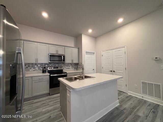 kitchen with a kitchen island with sink, appliances with stainless steel finishes, sink, and gray cabinetry