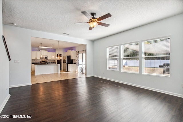 unfurnished living room featuring a textured ceiling, light hardwood / wood-style floors, a wealth of natural light, and ceiling fan