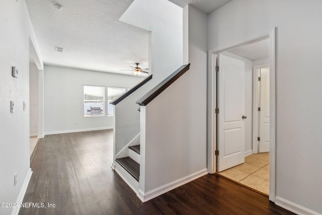 stairway with ceiling fan, wood-type flooring, and a textured ceiling