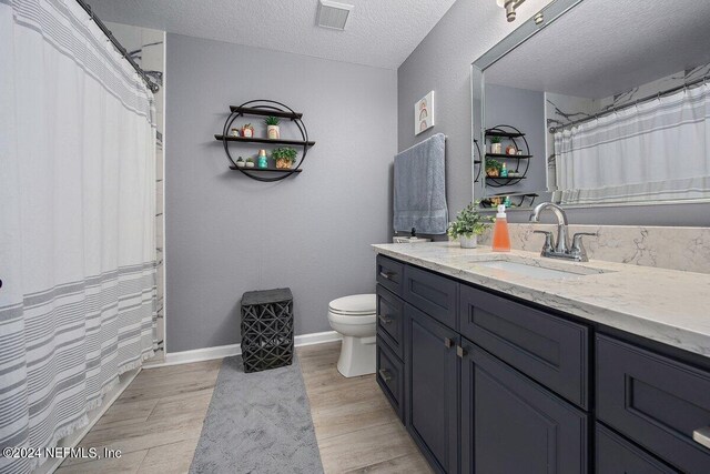 bathroom with vanity, a textured ceiling, walk in shower, toilet, and hardwood / wood-style floors