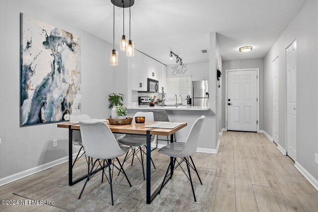 dining area featuring track lighting, a textured ceiling, and light hardwood / wood-style floors