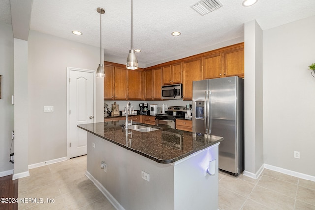 kitchen with dark stone countertops, a kitchen island with sink, sink, and stainless steel appliances