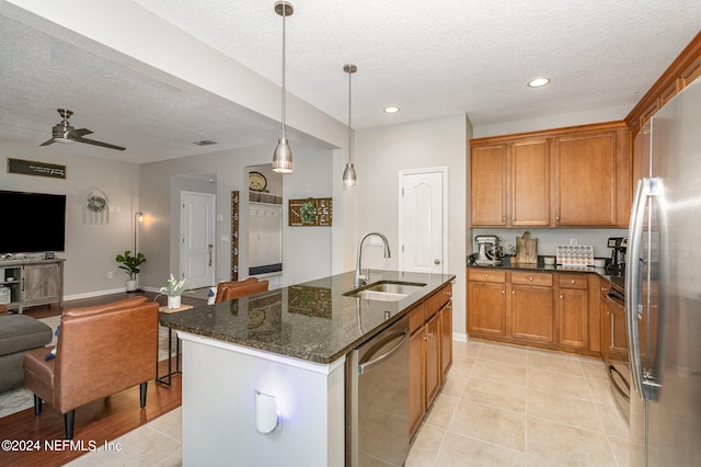 kitchen with appliances with stainless steel finishes, a textured ceiling, ceiling fan, a kitchen island with sink, and sink