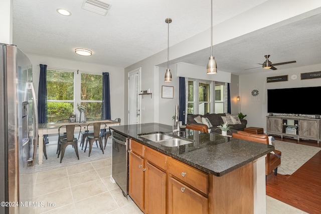 kitchen with stainless steel appliances, ceiling fan, decorative light fixtures, a center island with sink, and sink