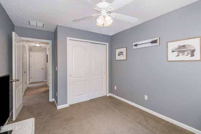 unfurnished bedroom with ceiling fan, light colored carpet, a textured ceiling, and a closet