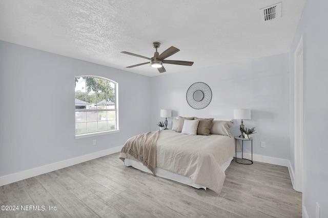 bedroom featuring light hardwood / wood-style floors, ceiling fan, and a textured ceiling