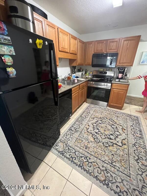 kitchen with light tile patterned floors, a textured ceiling, sink, and black appliances