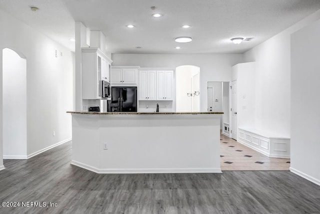 kitchen with white cabinetry, wood-type flooring, dark stone counters, and black fridge