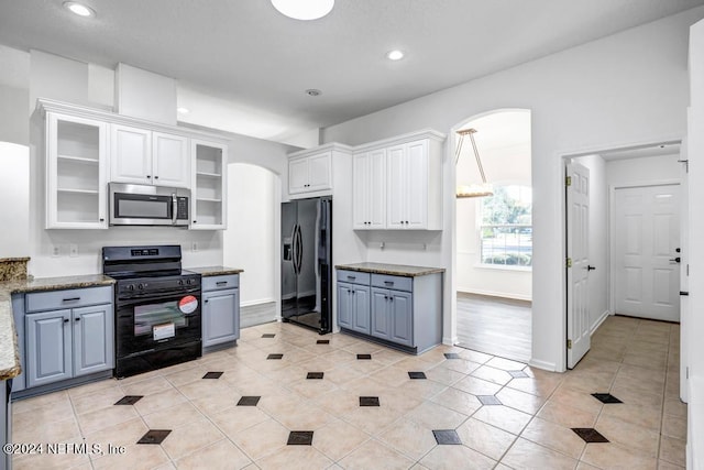 kitchen with light tile patterned flooring, white cabinetry, dark stone countertops, and black appliances