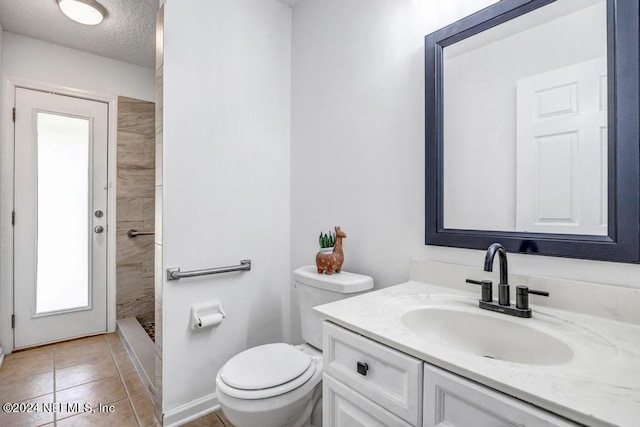 bathroom with tiled shower, tile patterned floors, toilet, vanity, and a textured ceiling