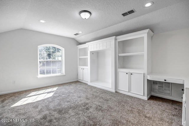 unfurnished bedroom with a textured ceiling, vaulted ceiling, and light colored carpet