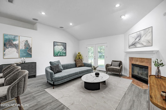 living room featuring french doors, a tiled fireplace, wood-type flooring, and lofted ceiling