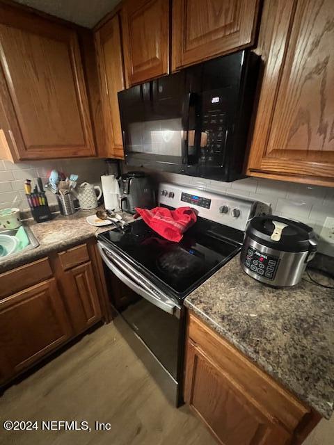 kitchen featuring decorative backsplash, dark stone countertops, electric range, and light hardwood / wood-style flooring