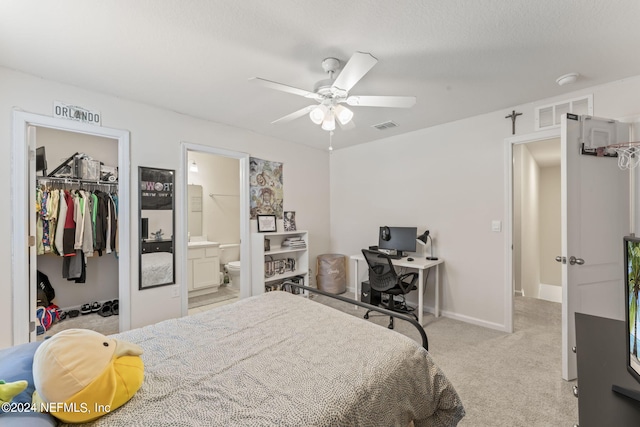 bedroom with ceiling fan, connected bathroom, a walk in closet, a closet, and light carpet