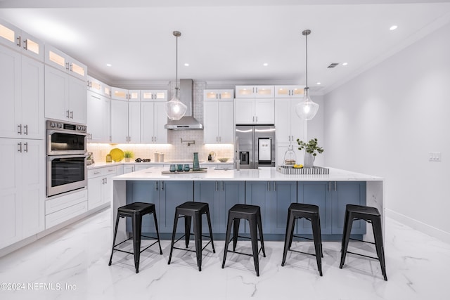 kitchen featuring appliances with stainless steel finishes, a large island with sink, pendant lighting, and wall chimney range hood