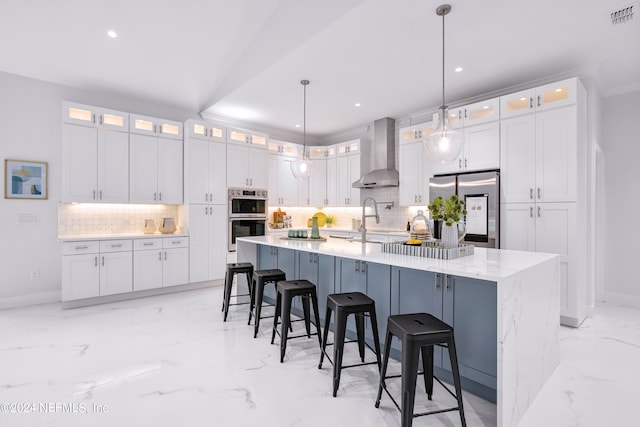 kitchen featuring white cabinets, decorative light fixtures, wall chimney range hood, stainless steel appliances, and a spacious island