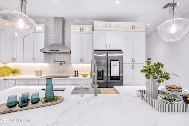 kitchen featuring white cabinets, hanging light fixtures, wall chimney exhaust hood, decorative backsplash, and stainless steel fridge