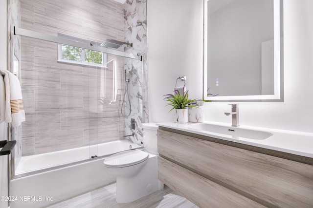 full bathroom featuring wood-type flooring, combined bath / shower with glass door, vanity, and toilet