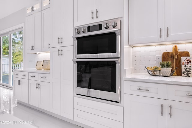 kitchen featuring stainless steel double oven, light stone countertops, decorative backsplash, and white cabinetry